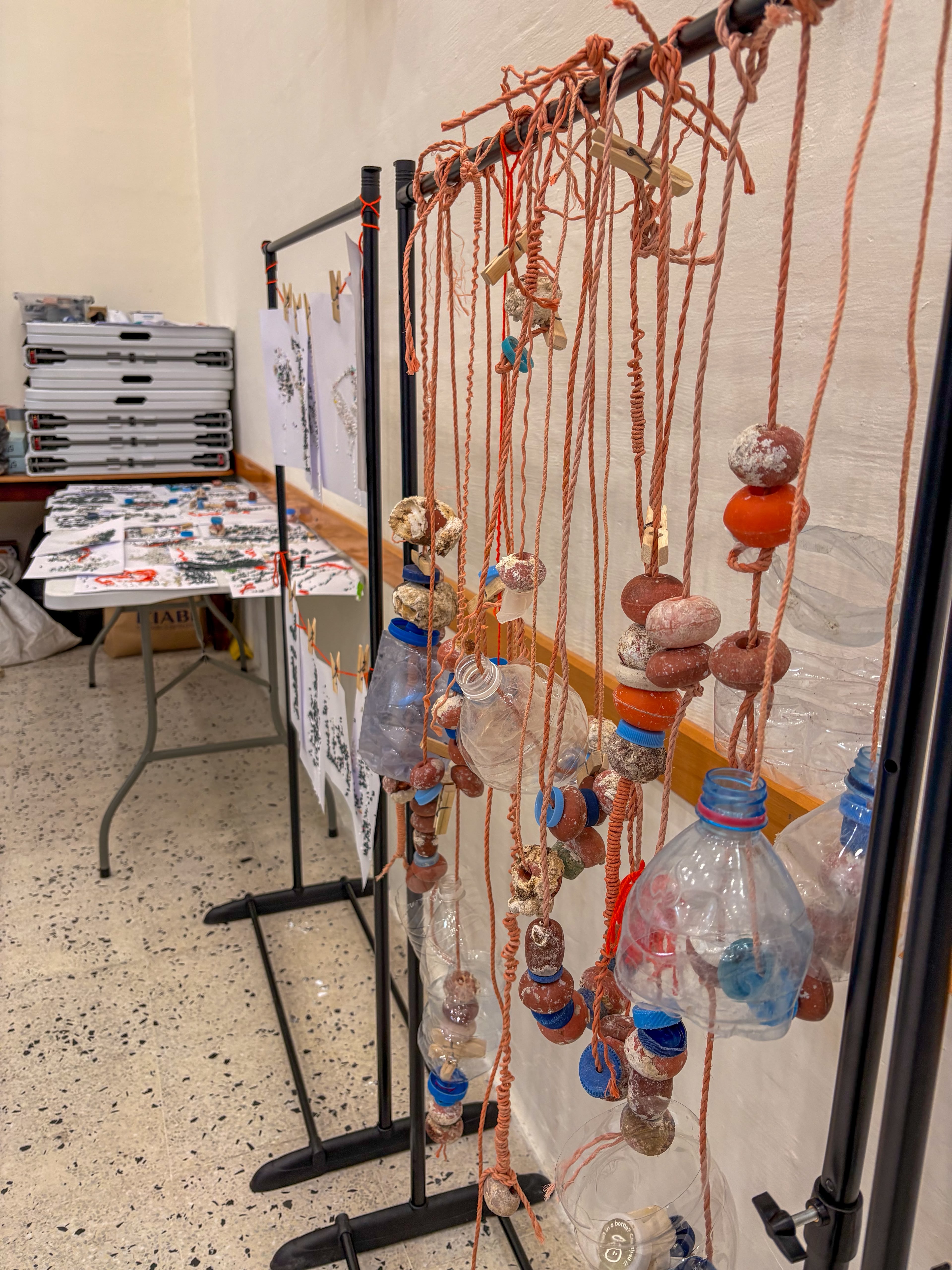 Hanging art pieces made by students from marine plastic — rope, bottle caps and recovered fragments — displayed on stands at FEE Fest, with children's drawings on a table behind.